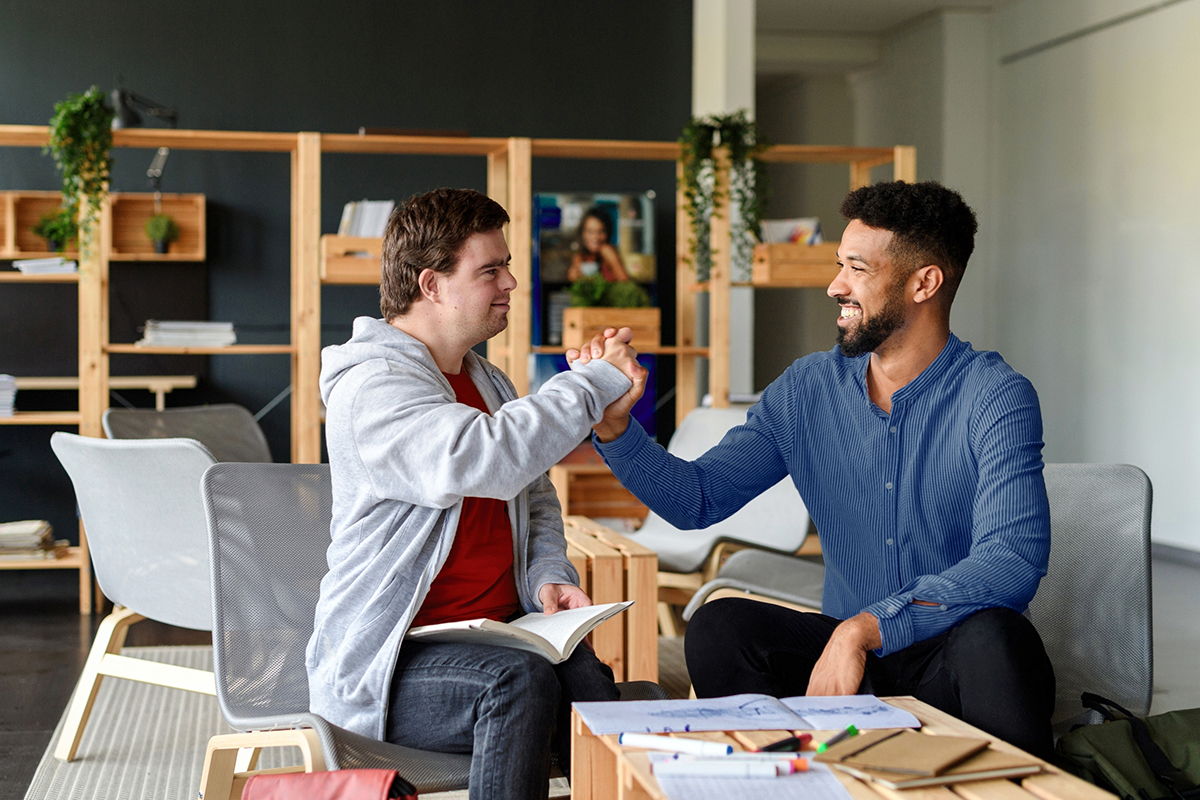 A direct support provider and patient give each other a high-five while sitting at a craft table
